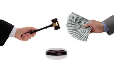 one hand holding judge's gavel, the other holding hundred dollar bills