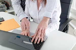 Man putting hands on female coworker's hands at computer