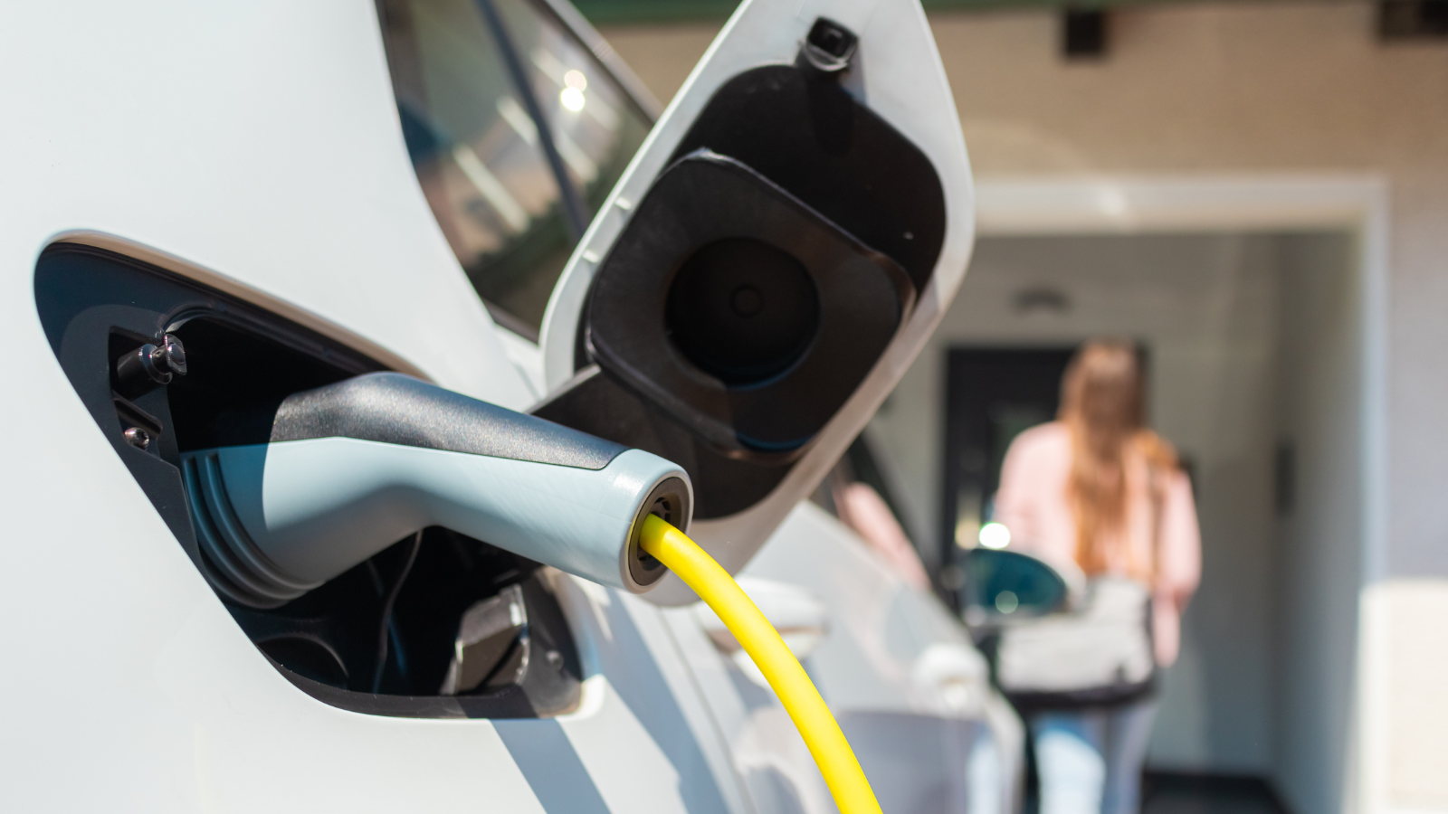 White EV charging with woman walking away in background