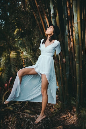 Woman in dress with smooth legs standing by bamboo.