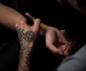Man with tattoo sketching another tattoo on a wrist.