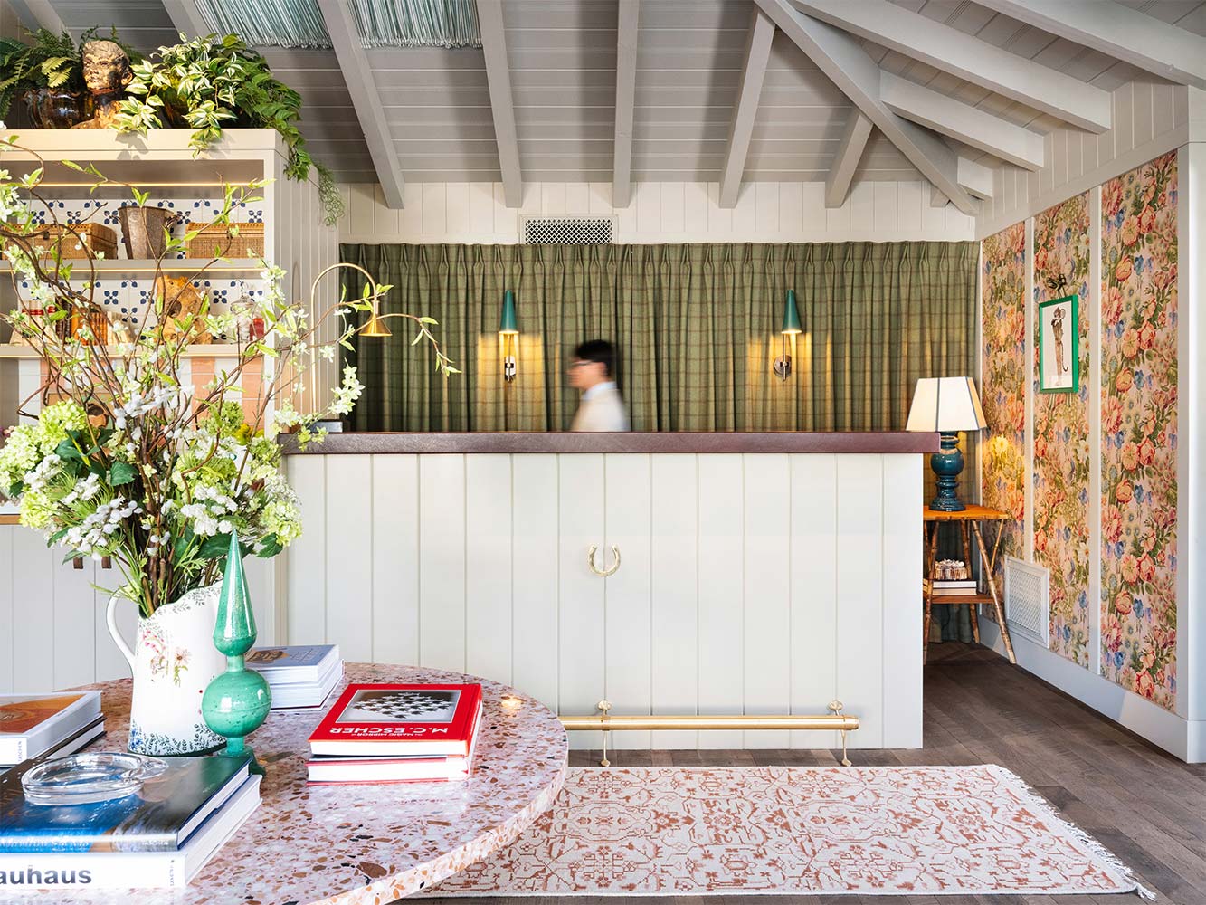 A lobby with a reception desk, books, flowers, and decorative wallpaper.
