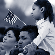Hispanic Girl Waves an American Flag while on a man's shoulders