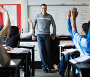 Photo of a teacher and a class of students raising their hands.