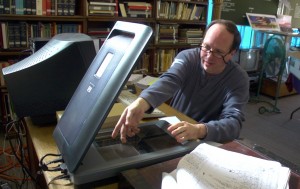 Man in glasses digitizing documents using a flatbed scanner.