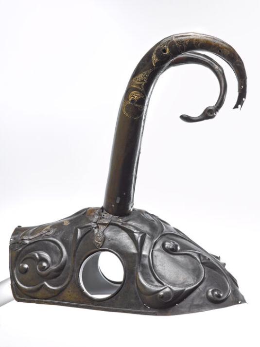 A metal helmet for a horse features two round holes for the horse's ears and two curved horns on top.