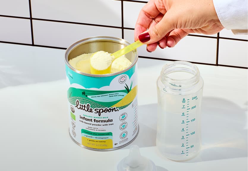 A hand scoops Little Spoon infant formula into a baby bottle