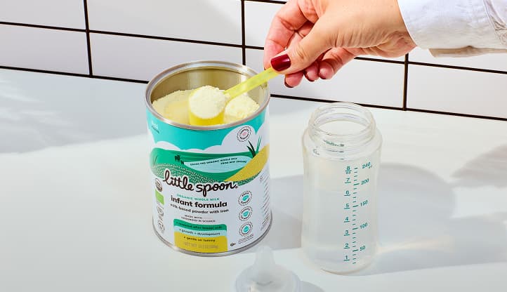 A hand scoops Little Spoon infant formula into a baby bottle