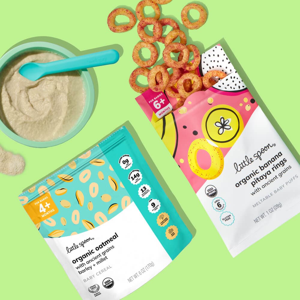 Overhead view of resealable bag of baby cereal next to a light blue bowl full of prepared baby cereal and a resealable bag of baby puffs, against a light green background