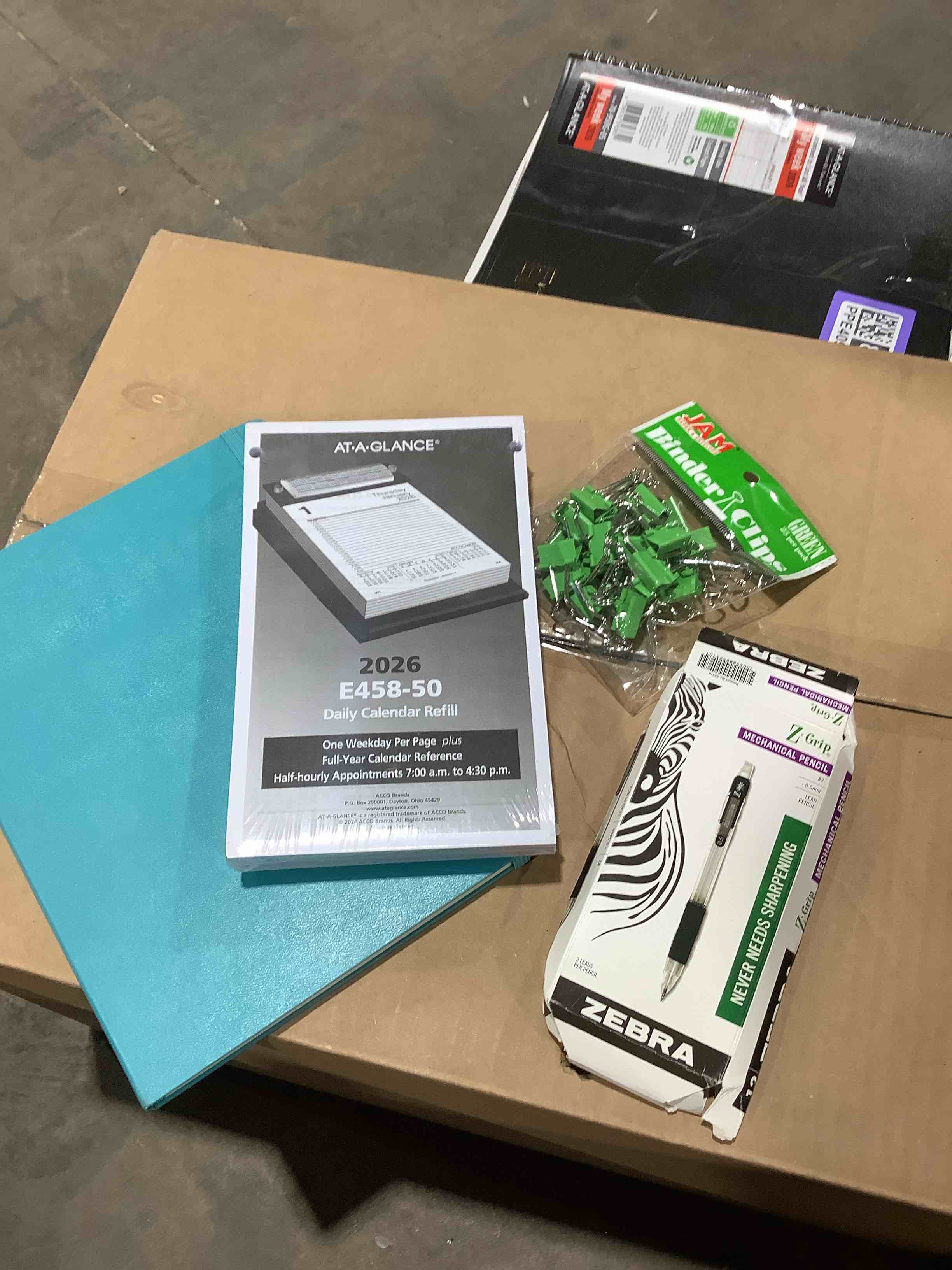 assorted office supplies: at a glance 2026 calendar, refill, binder clips, zebra pencils, and teal notebook