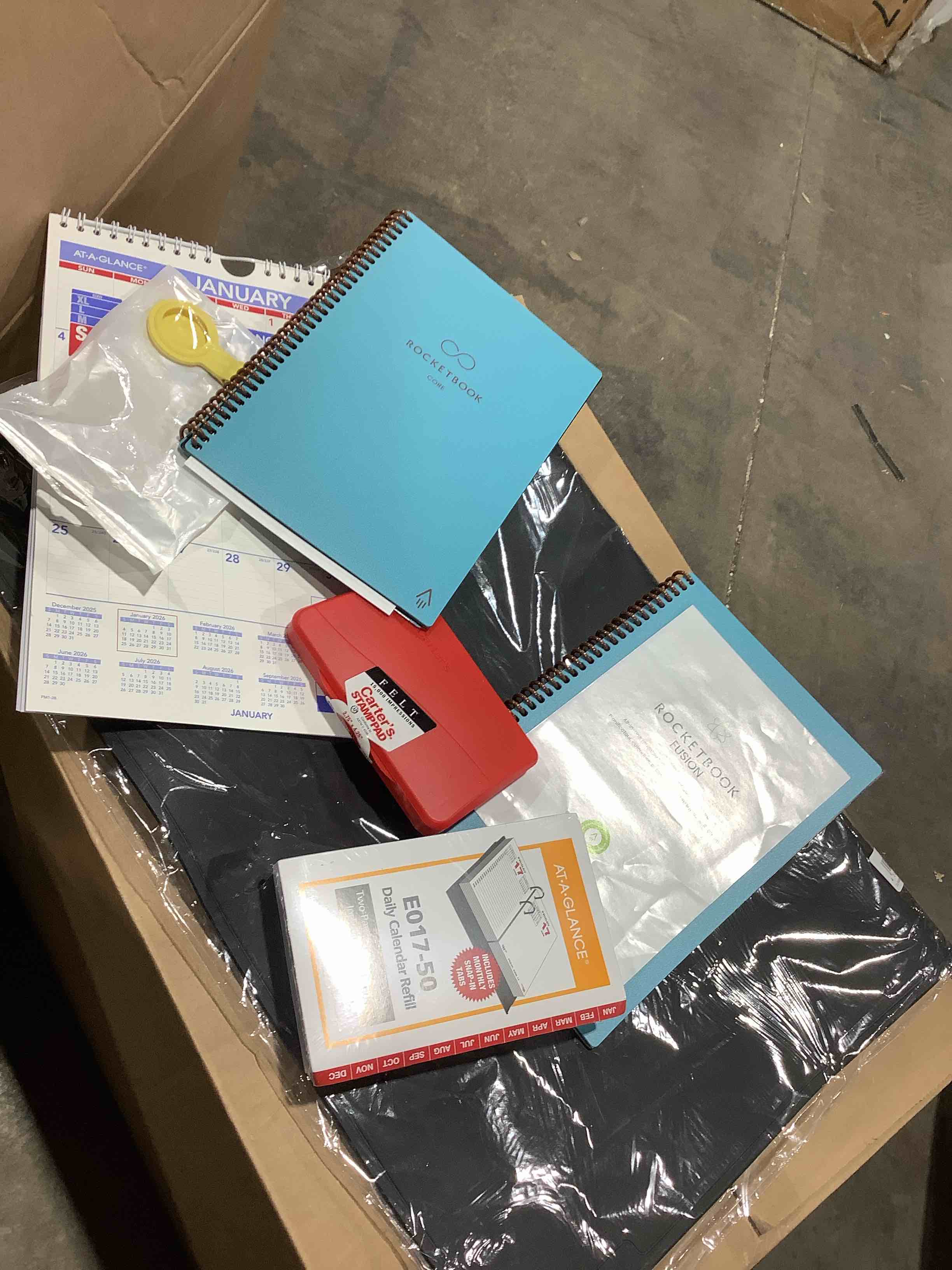 Assorted office supplies: at a glance daily calendar, refill, rocket book fusion, Carter's stamp pad, January 20 26 calendar, notepad for top of desk