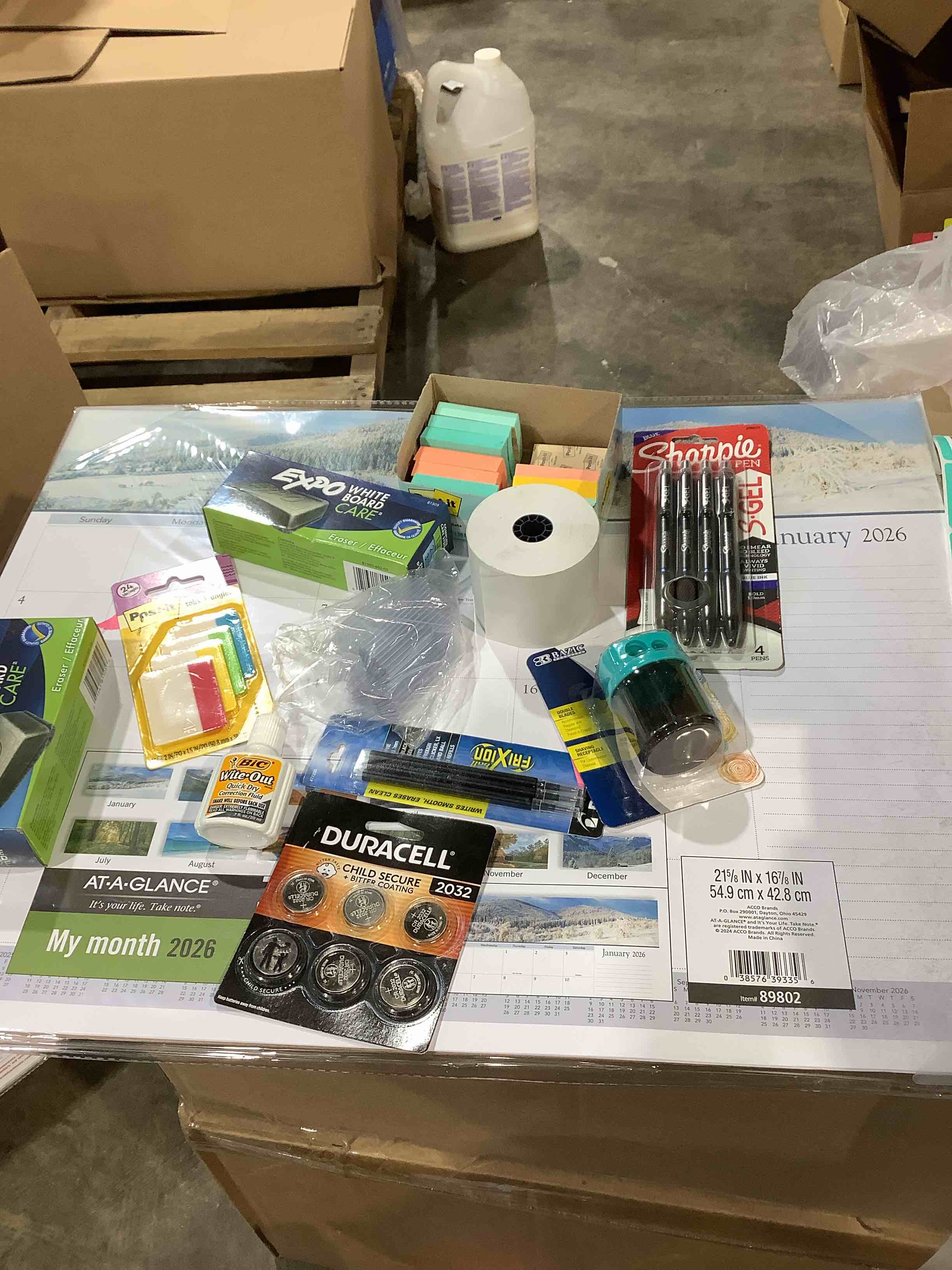 assortment of office supplies: post-it notes, sharpie pens, duracell batteries, 2026 desktop calendar and much more