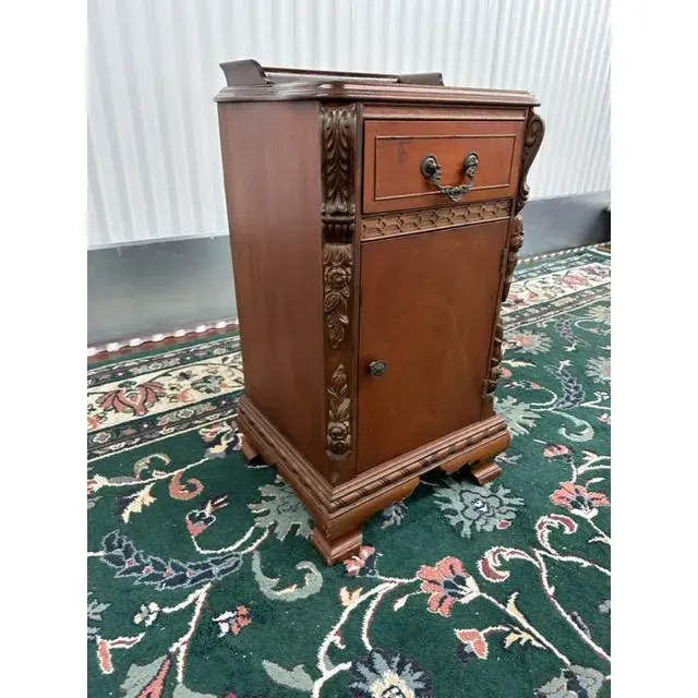 Late 19th Century Style Rich Cherry Wood Antique Ardsleigh Nightstand, with an Open Space Base Cabinet, Drawer, Gold Brushed Brass Floral Accent Handle and Knob, and Hand Carved Wooden Accents. Custom made, stock photos differ from piece. Buy/Repair Drawer sides need fixed, and wooden slab needed for top. Exterior in beautiful condition. 24” W x 35” D x 29” H 