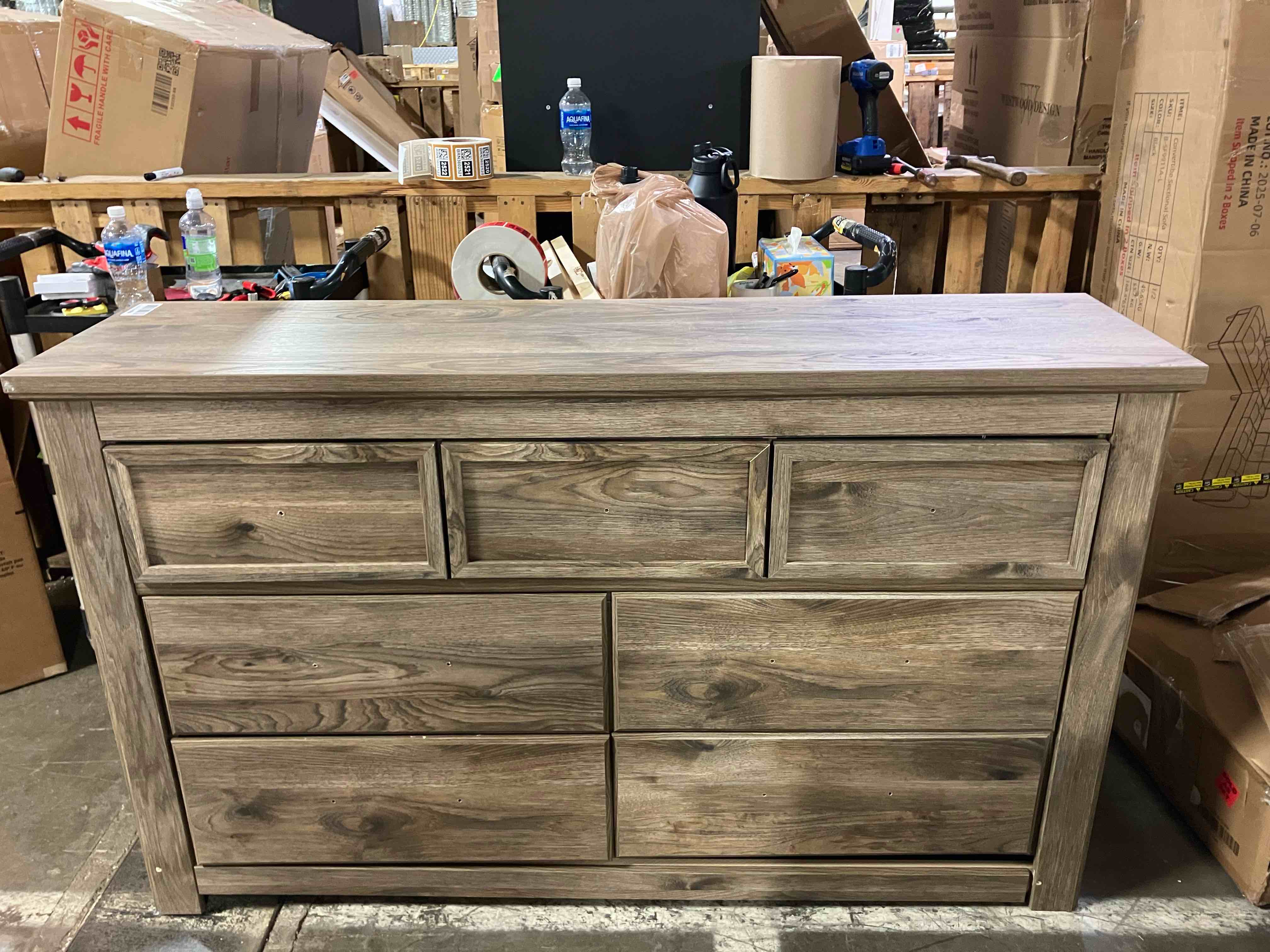Condition photo showing As Is for Rusticott Dresser Seven Drawer Dresser By Ashley Signature Design - (As is because of damage to bottom drawer tracks, the top center drawer, and bottom base plate. Buy and Repair)