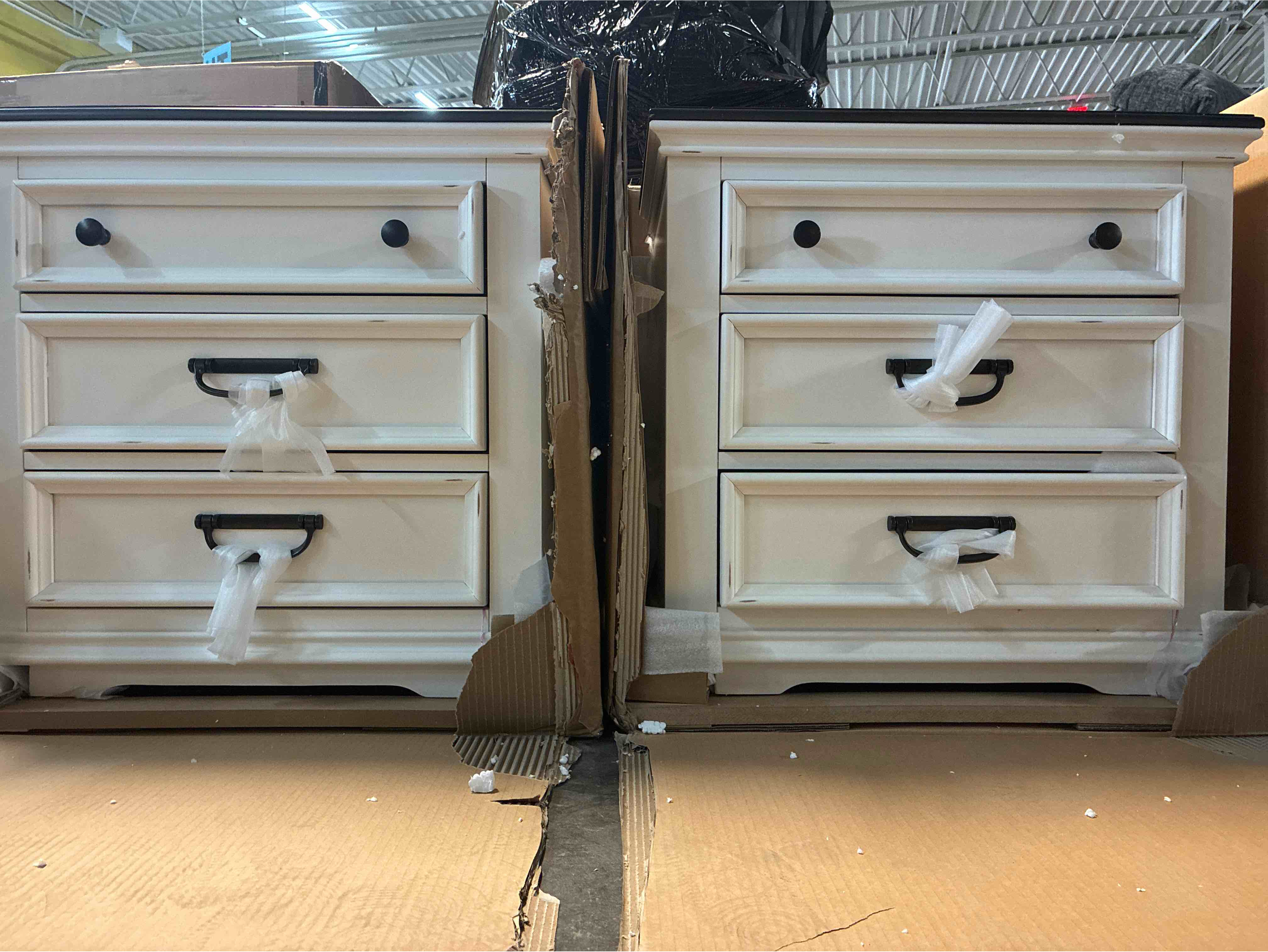 Condition photo showing New/Like New for Semaj 2 Tone Distressed White and Rustic Brown 3 Piece Solid Wood Bedroom Set with 9 Drawer Dresser, Two 3 Drawer Nightstands, Matte Black Metal Handles/Knobs. 1 1.5” Hairline scratch along top edge of left nightstand, otherwise brand new. Nightstands: 28.3'' H X 26.3'' W X 17.4'' D Dresser: 38.6'' H X 63'' W X 17.4'' D