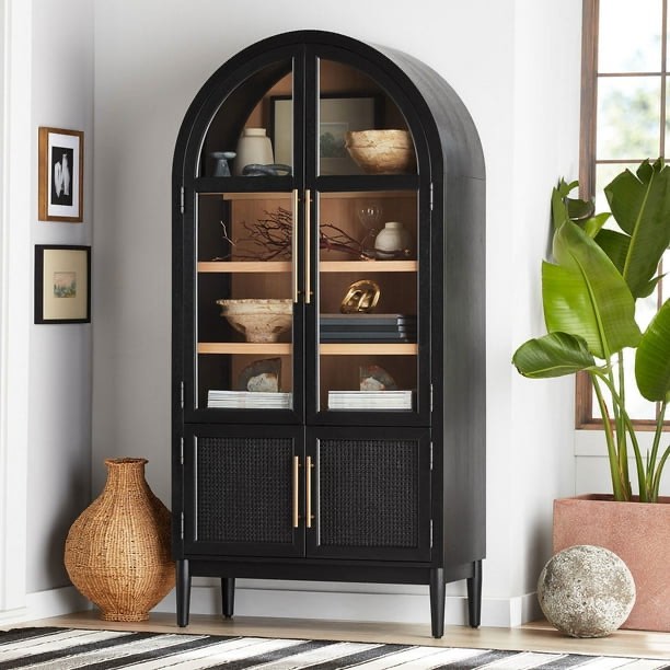 Member's Mark Enzo Storage Cabinet With Rattan Cabinet Doors in Black with Gold Brushed Metal Handles, Arched Glass Doors, Open Space Base Cabinet, and 4 Tier Shelves. 