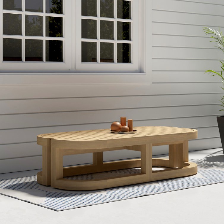 Emory Acaica Wood Coffee Table With Light Teak Finish. Weather, water, & UV Resistant. 15'' H X 27'' D X 55'' W . Hairline scratch on bottom leg otherwise beautiful condition