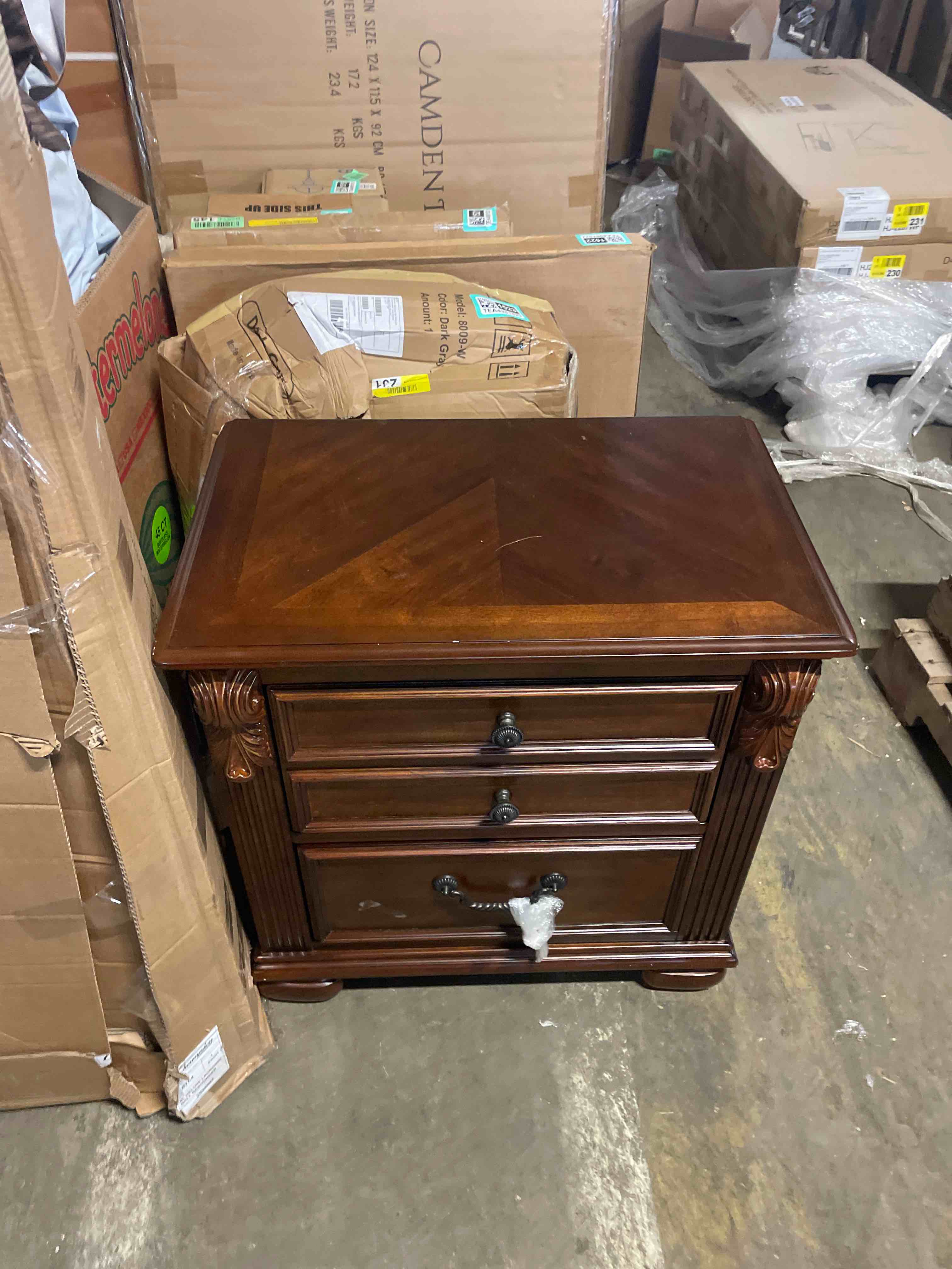 Condition photo showing New/Like New for homestock vogue cherry oak brown 25 x 16 x 28 inch nightstand with 3 drawers brass accents bun feet and dark toned handles classic appeal