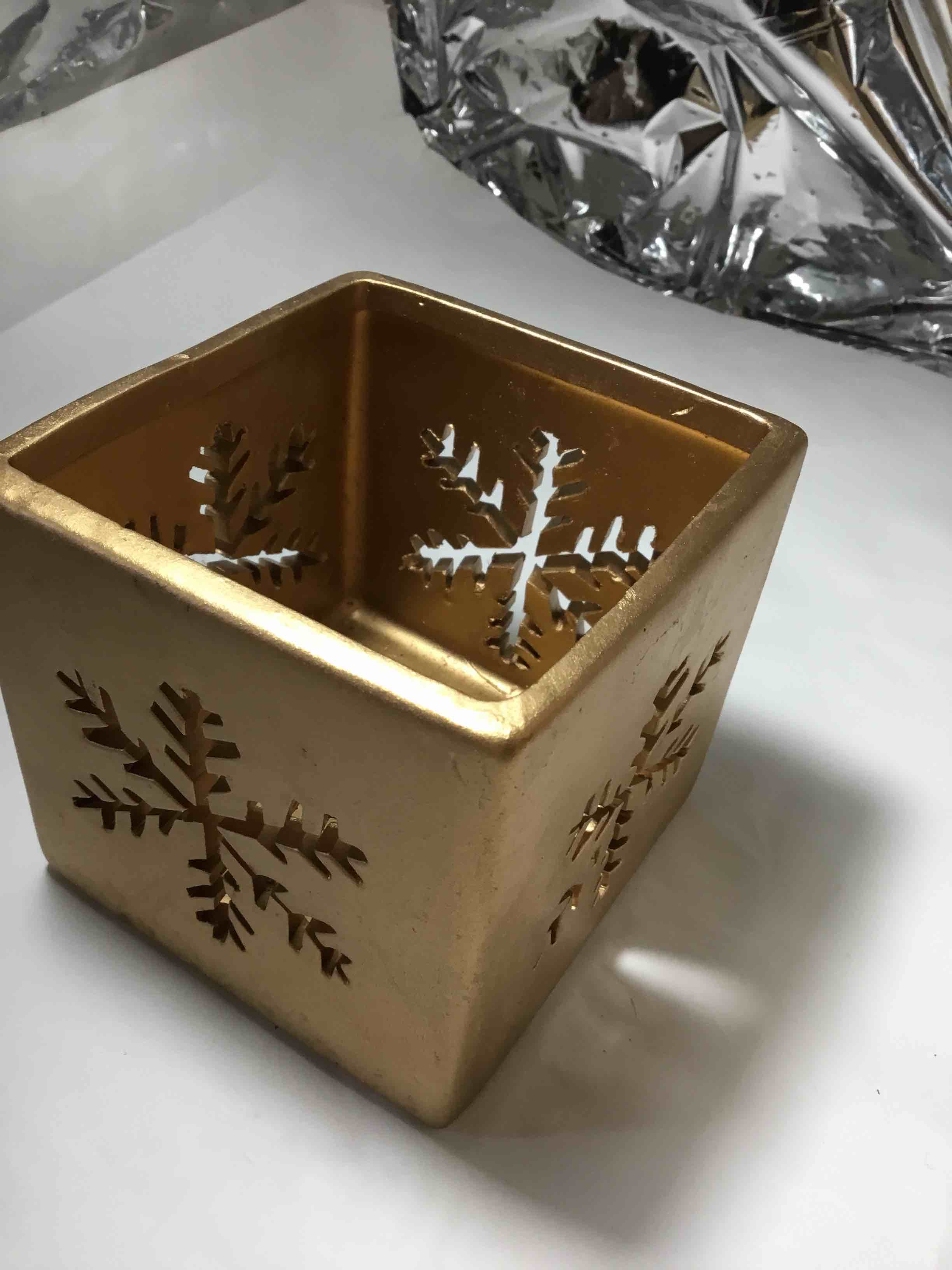 Gold-colored ceramic cube candle holder with snowflake cutouts.