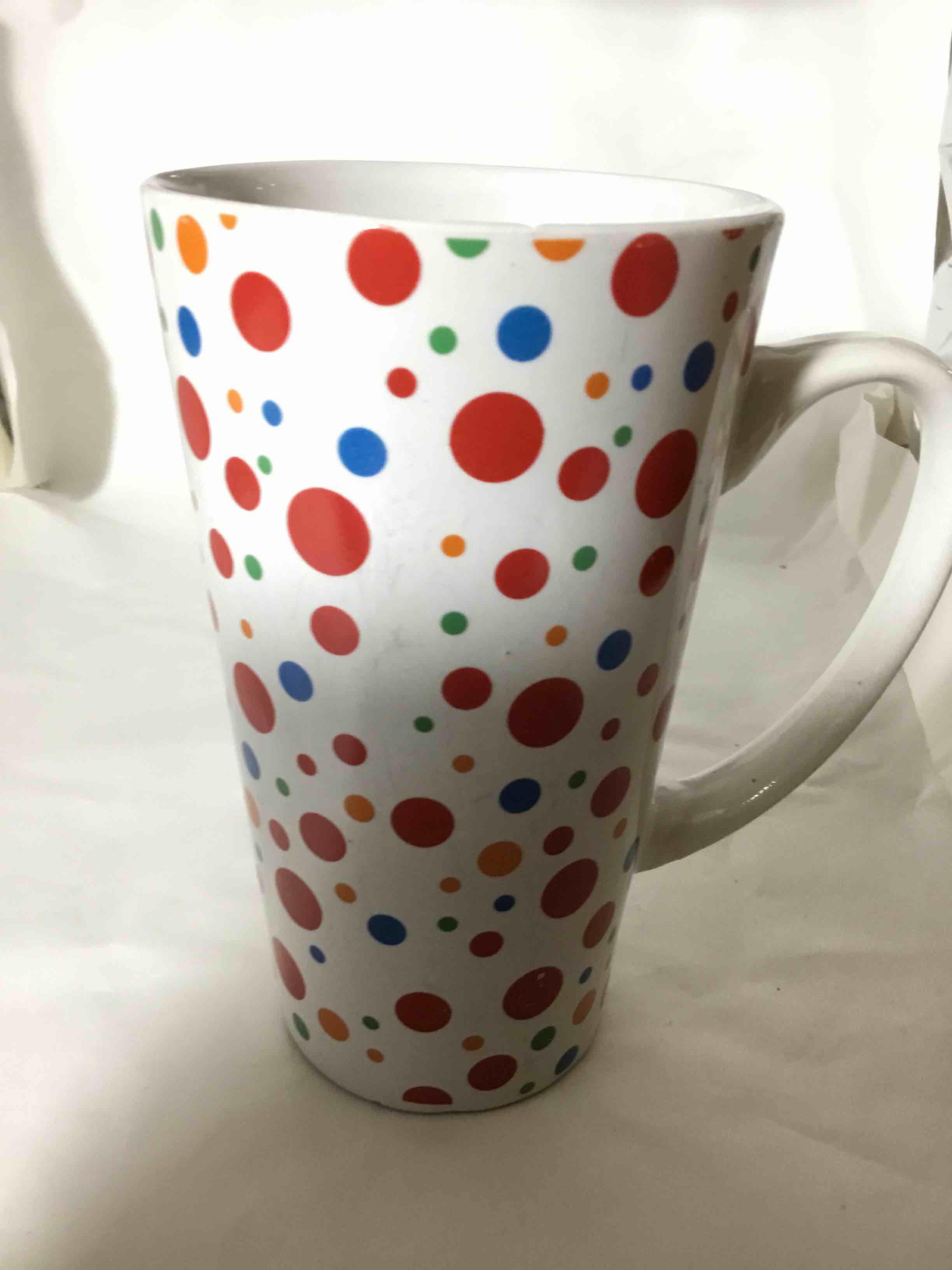 Tall mug with bright, multi-colored polka dots or sprinkles on a white background