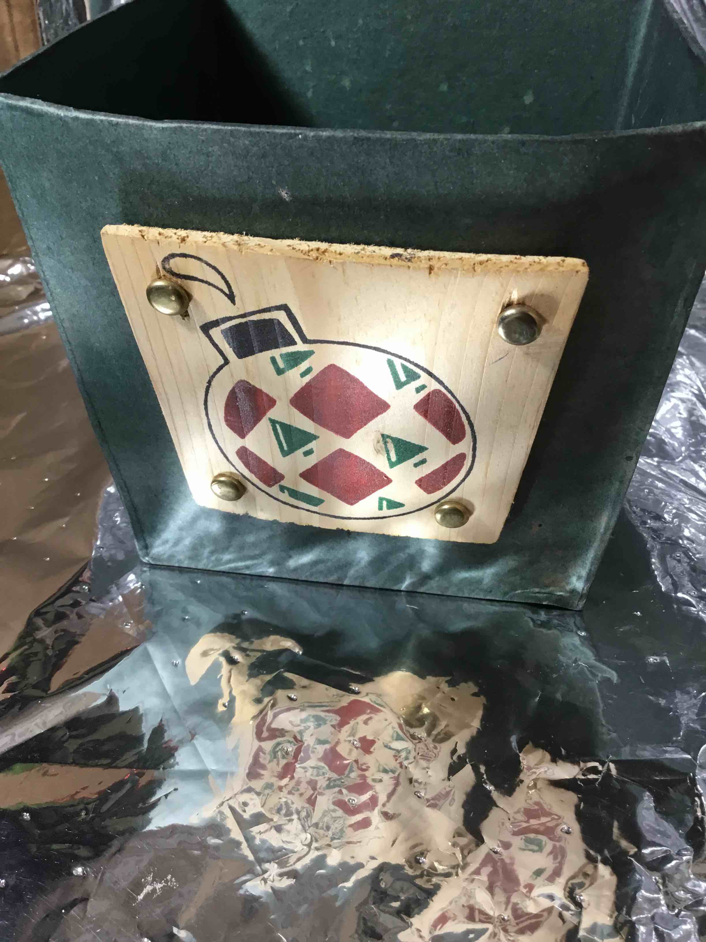 Christmas container or basket, papier-mâché with a green finish. It is decorated with a wooden plaque featuring a painted Christmas ornament design.