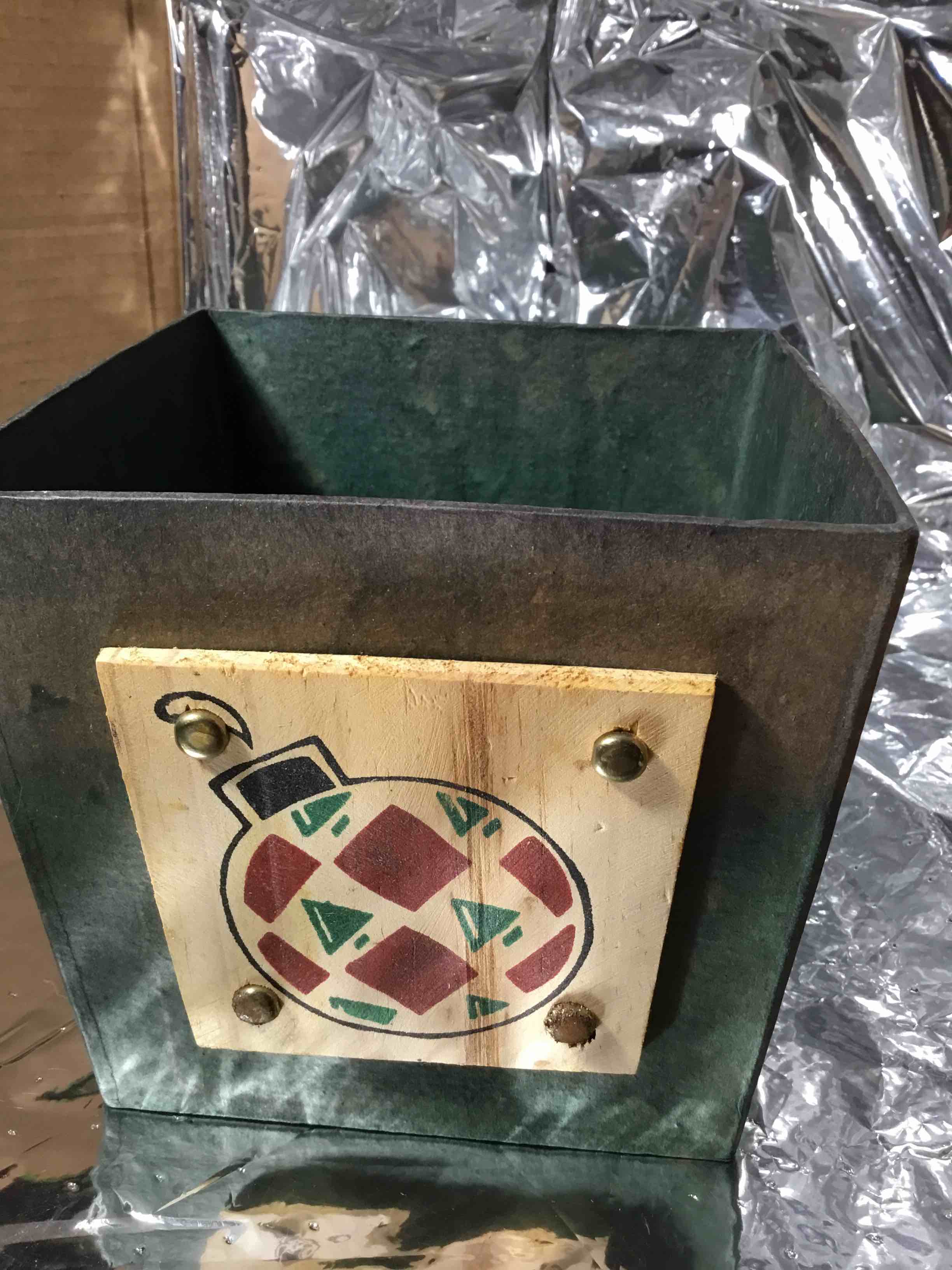 Christmas container or basket, papier-mâché with a green finish. It is decorated with a wooden plaque featuring a painted Christmas ornament design. 