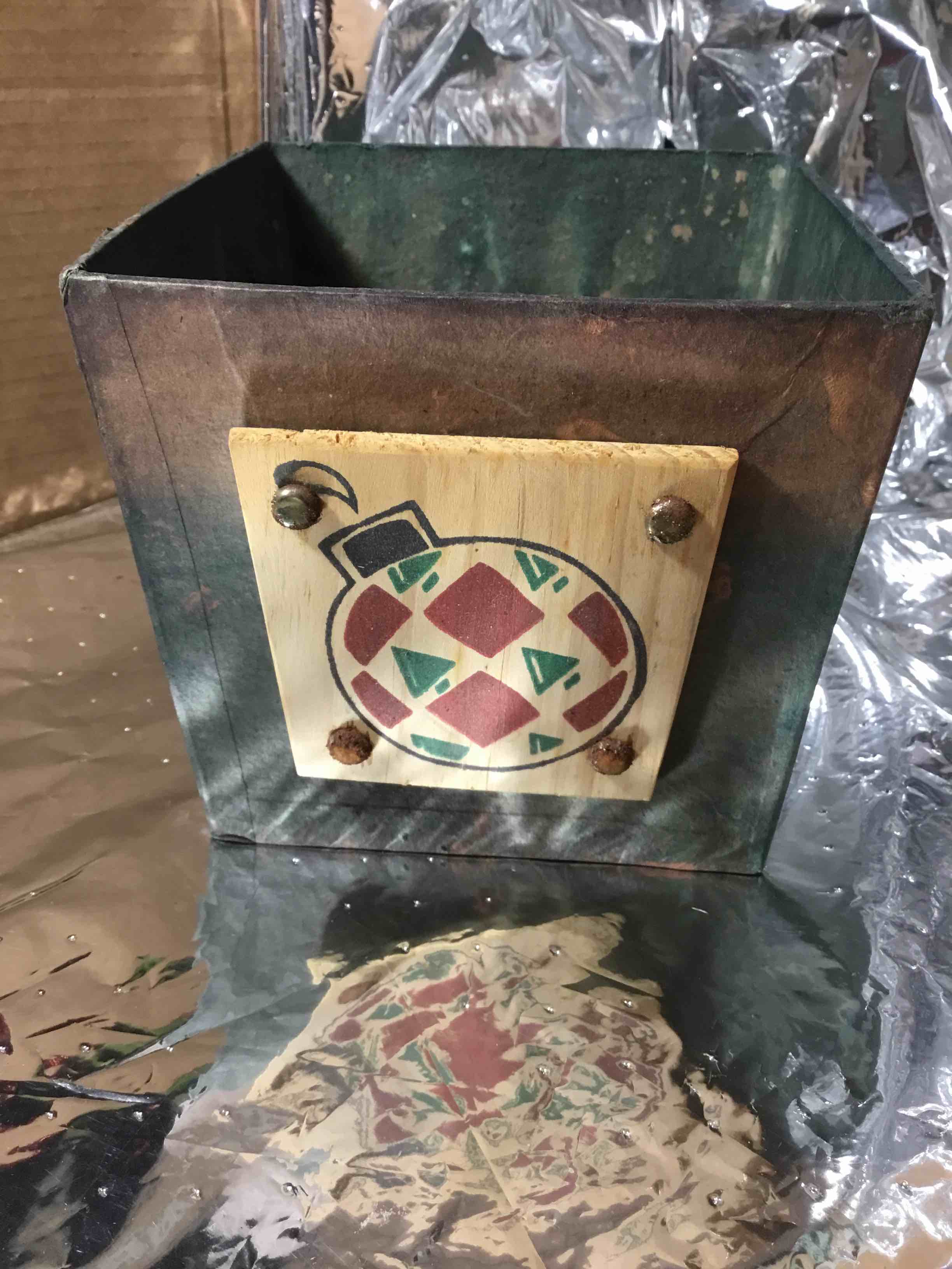 Christmas container or basket, papier-mâché with a green finish. It is decorated with a wooden plaque featuring a painted Christmas ornament design. 