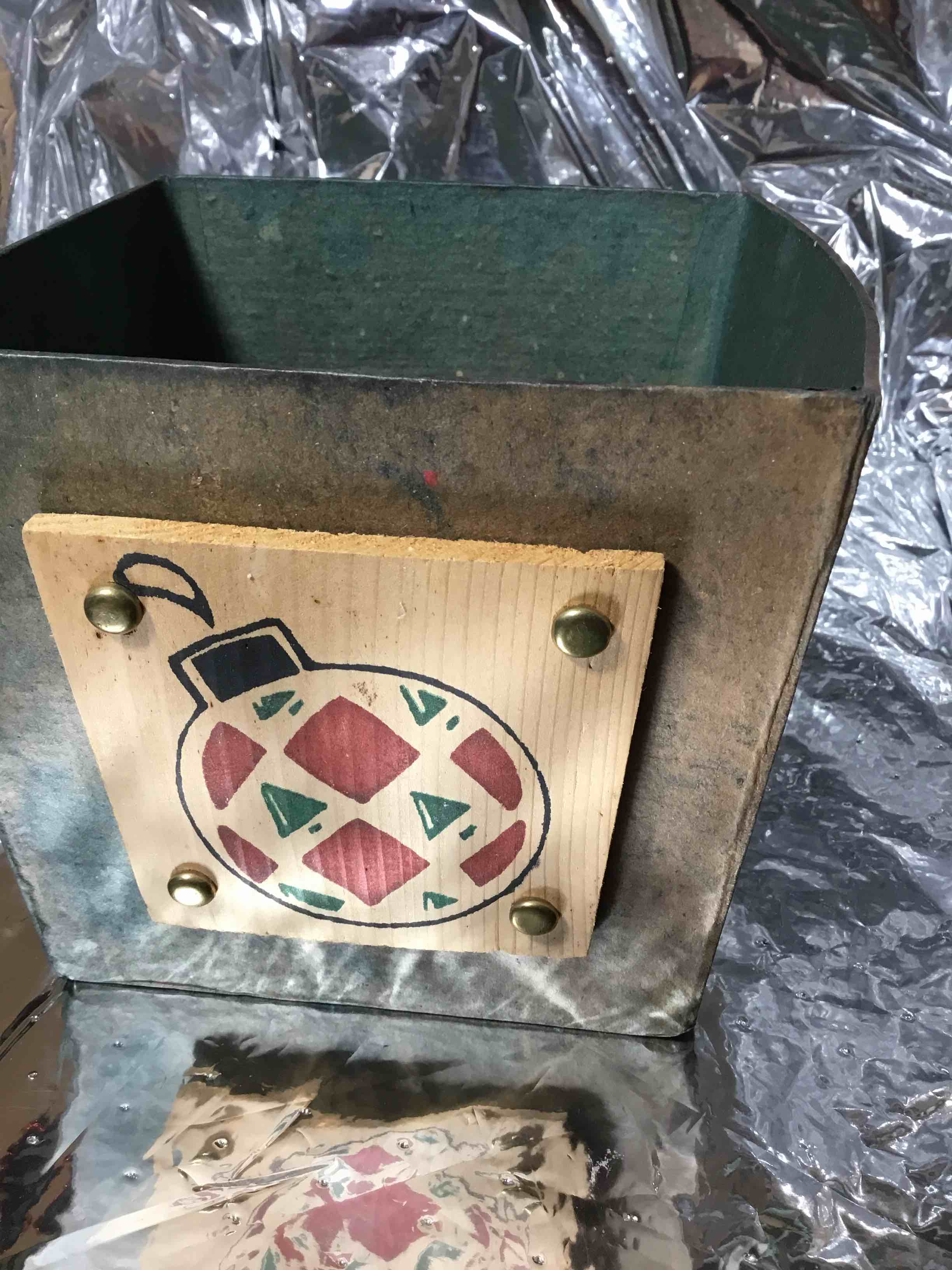 Christmas container or basket, papier-mâché with a green finish. It is decorated with a wooden plaque featuring a painted Christmas ornament design. 