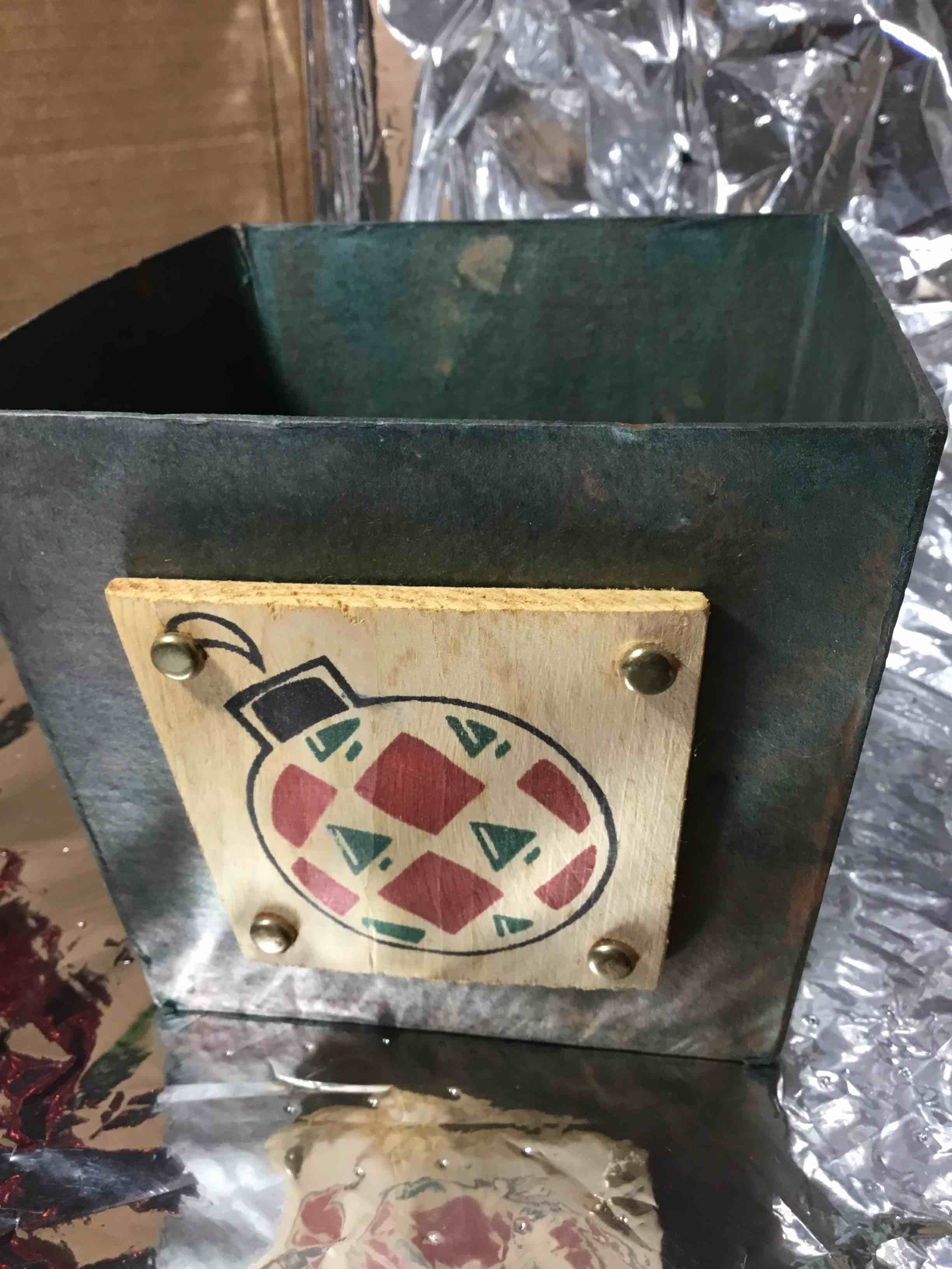 Christmas container or basket, papier-mâché with a green finish. It is decorated with a wooden plaque featuring a painted Christmas ornament design. 