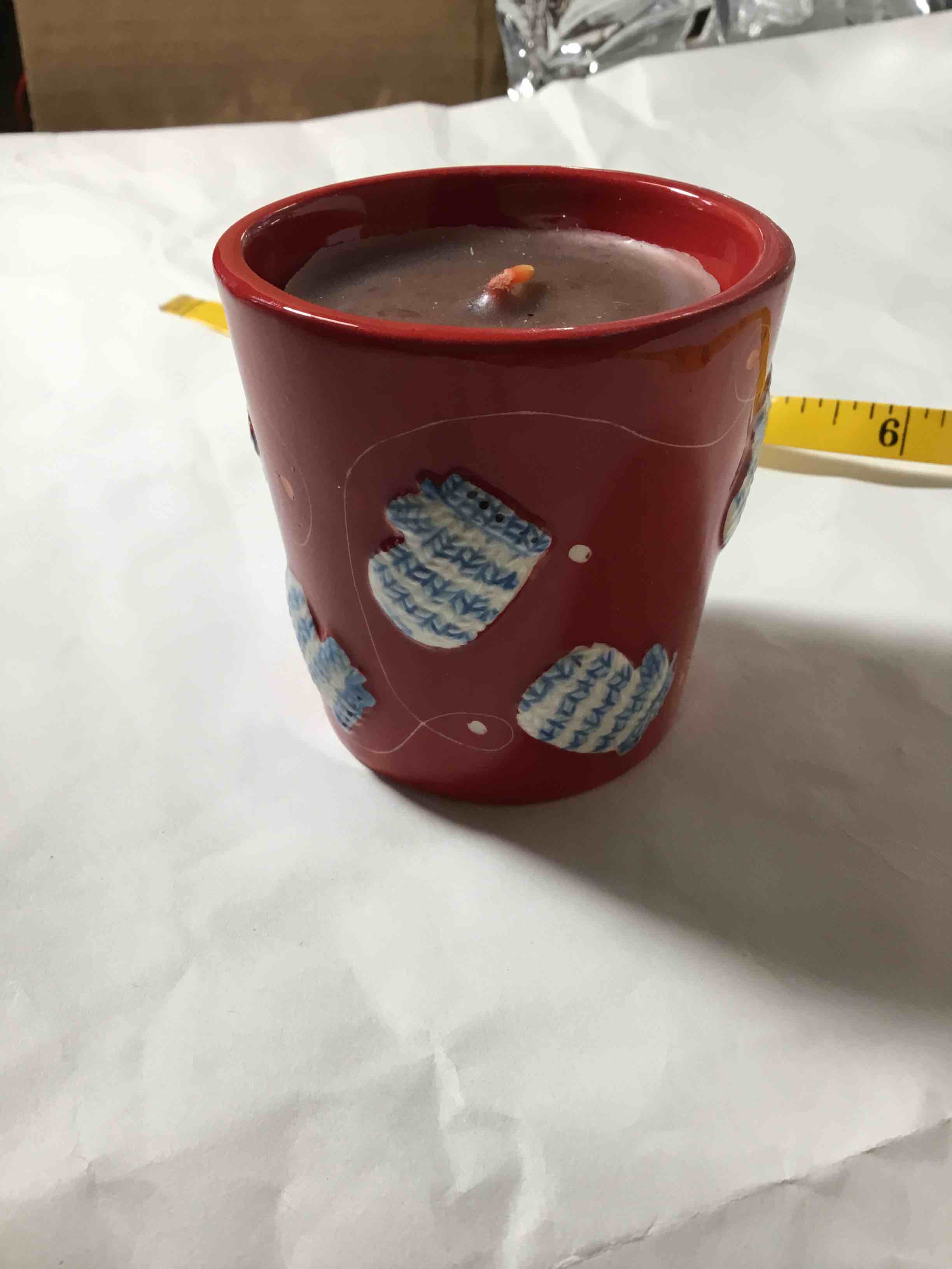 Scented candle in a red ceramic mug with a white and blue knitted mitten pattern