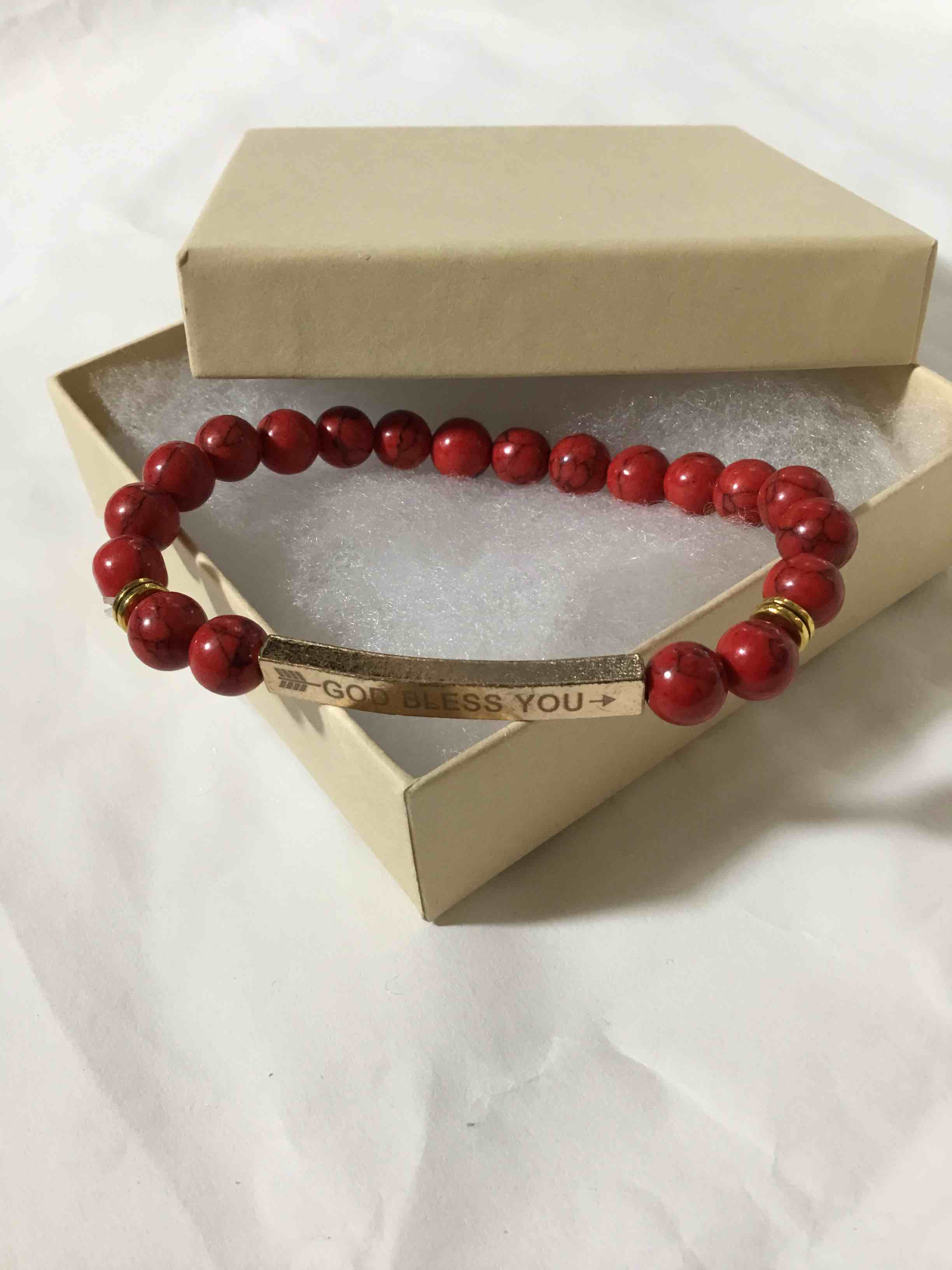 Red beaded stretch bracelet with a gold-tone bar engraved with "GOD BLESS YOU"