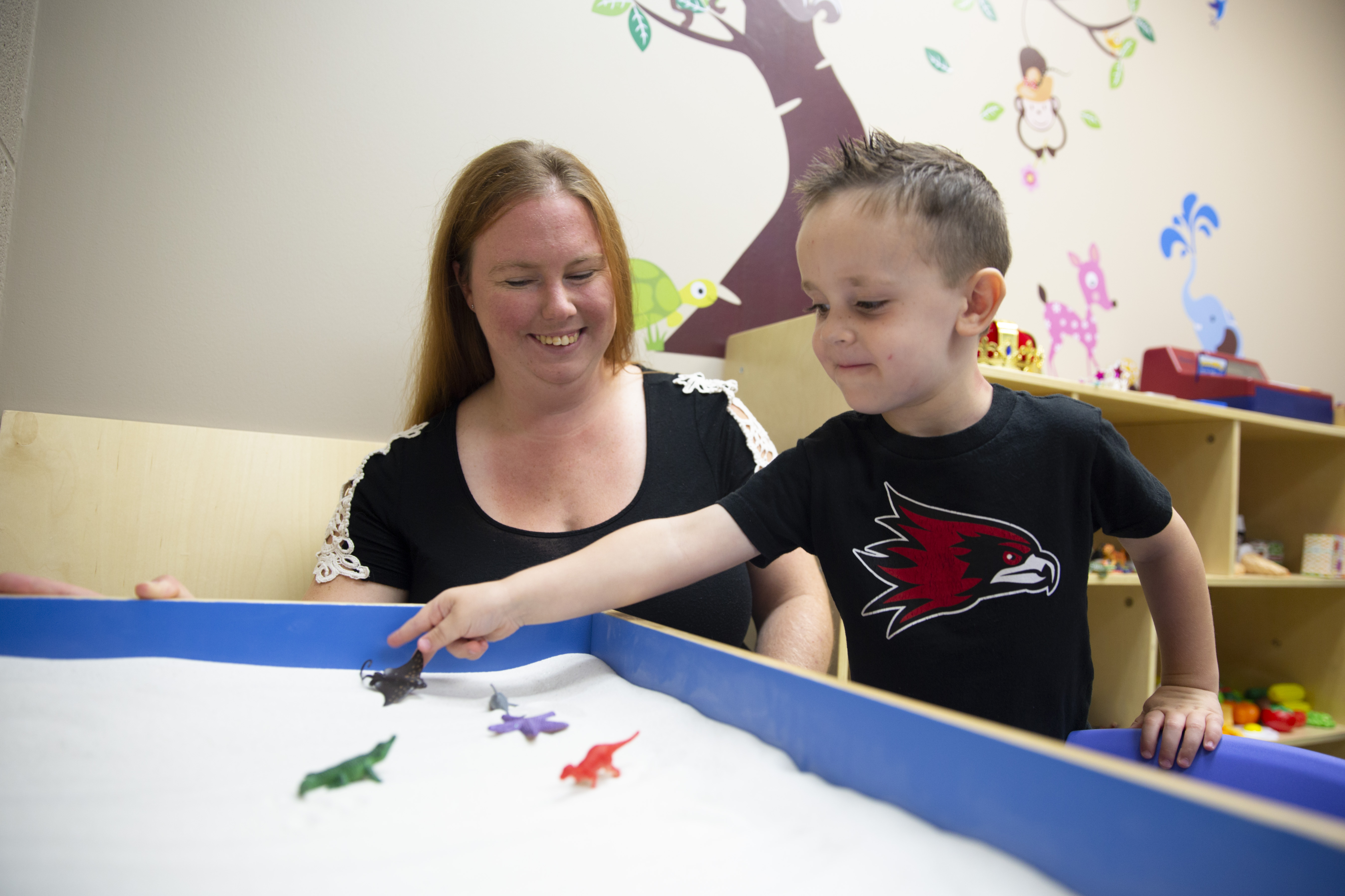 A woman smiling while helping a child playing in a sandbox 