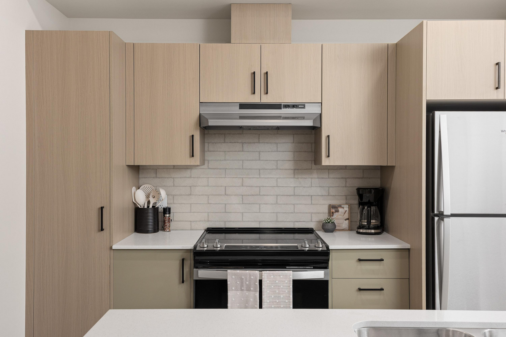 Alternate Angle: Modern kitchen at Central Kelowna featuring light cabinetry, tile backsplash, and open layout connecting to the dining area in an uptown apartment.