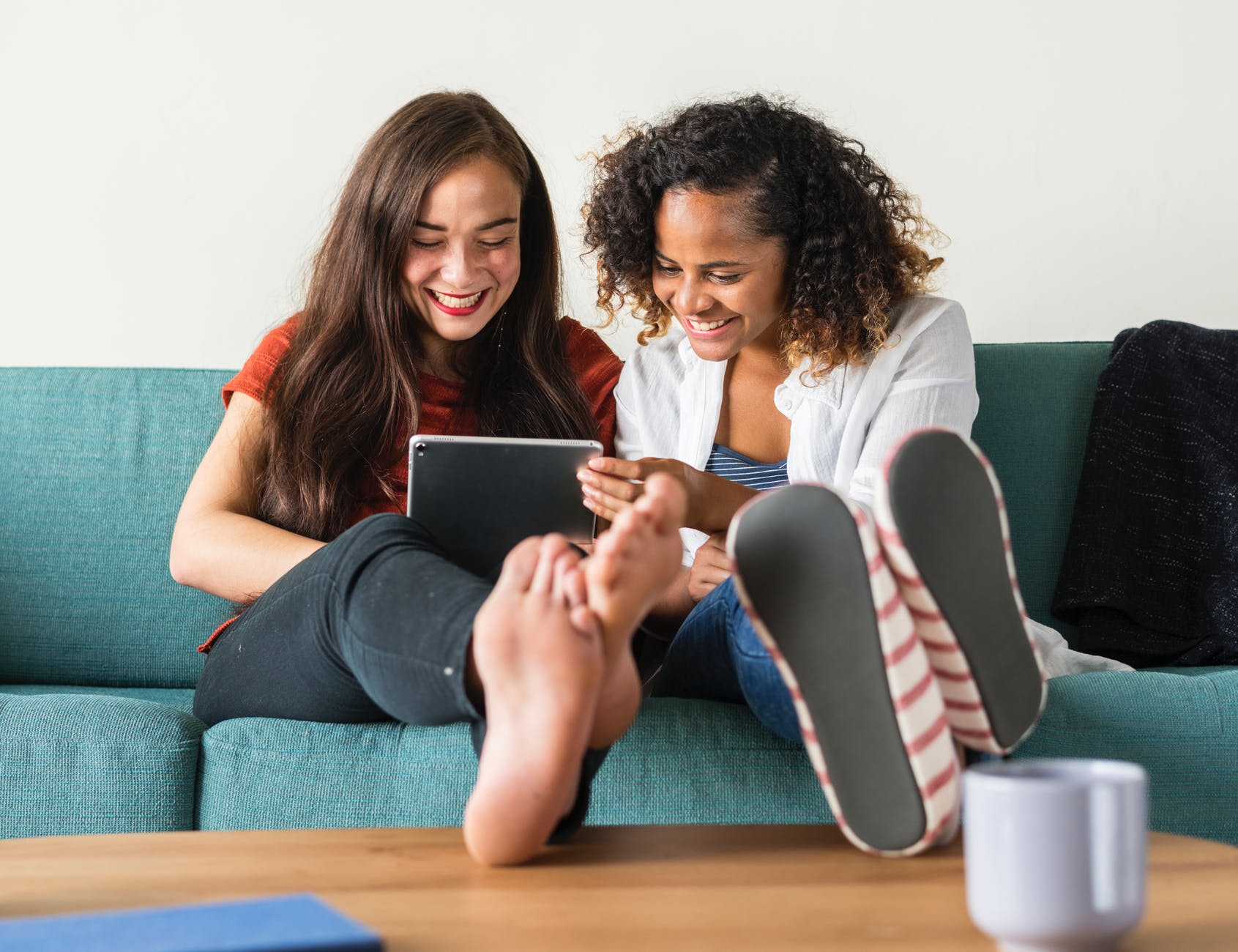 Two women sitting on a couch with a tablet.