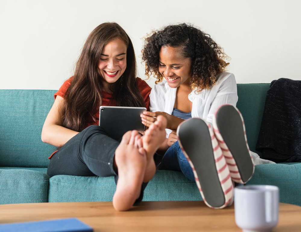 Two women sitting on a couch with a tablet.