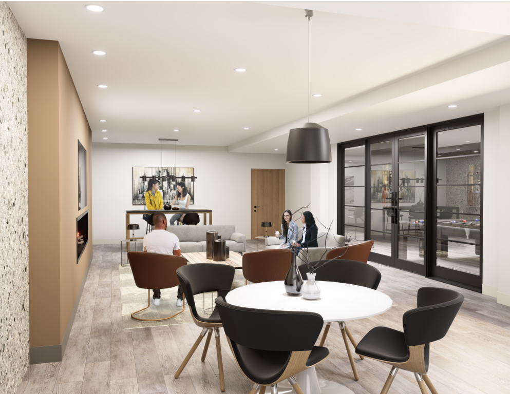 A spacious community lounge at The Vantage with residents socializing in various seating areas. To the left, a man sits by a linear fireplace embedded in a tan wall. In the center, two women chat on a grey sofa, while others sit at a high-top table in the 