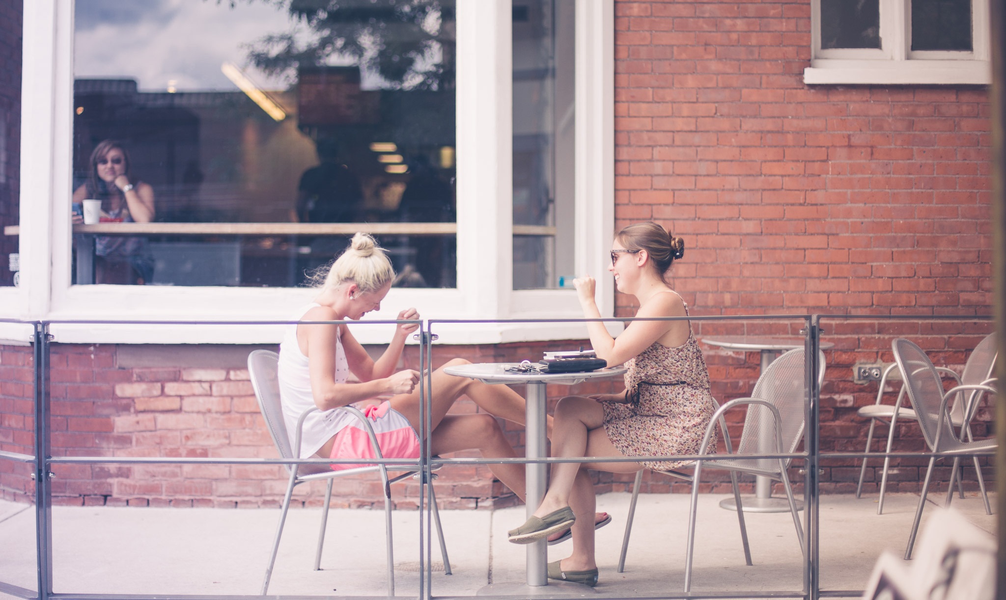 Sunlit patio catch‑up: two friends share coffee and conversation on a cozy café terrace in the city.