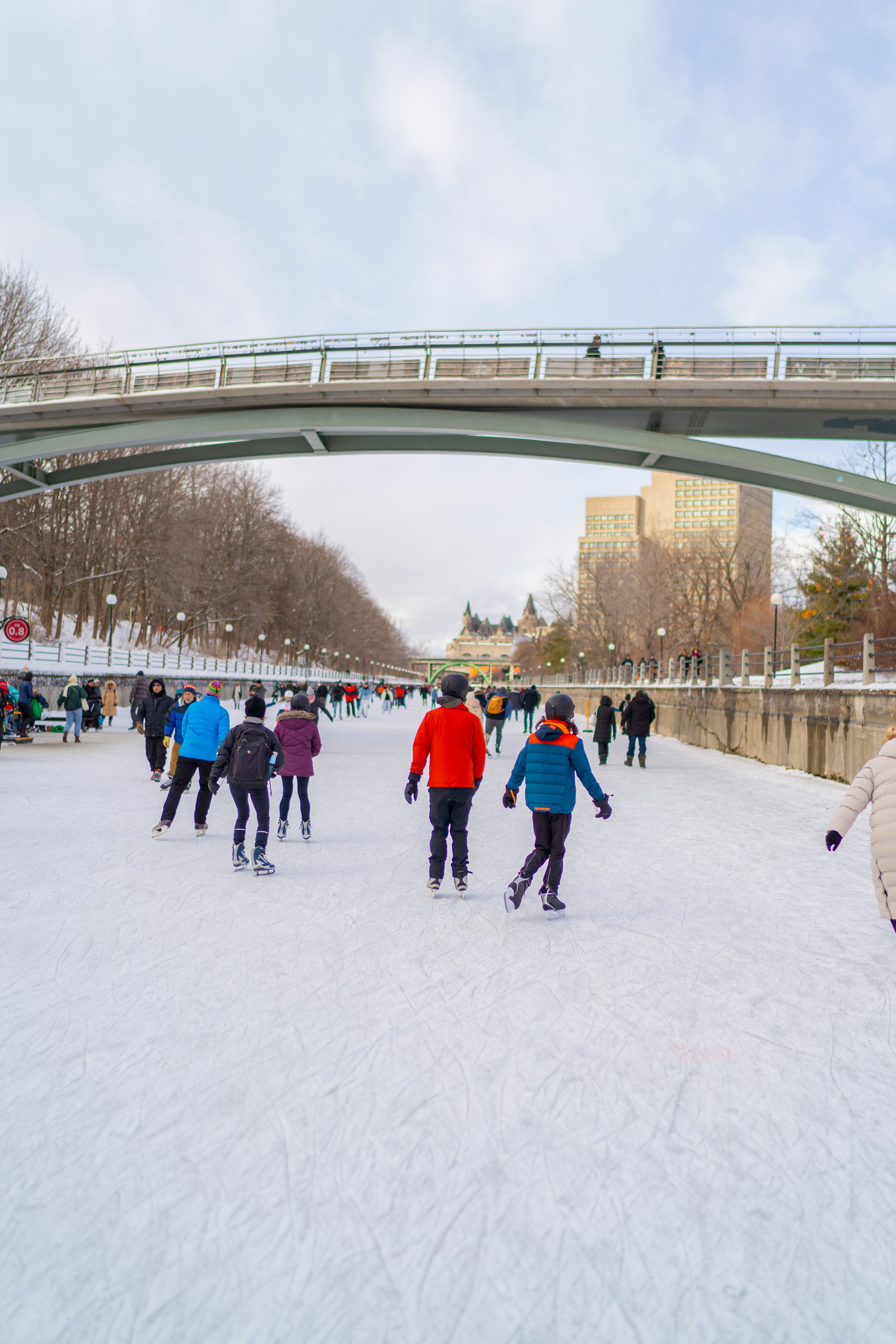 Winter magic on the Rideau Canal: skaters glide under a pedestrian bridge, taking in iconic downtown Ottawa views on the world‑famous skating rink.