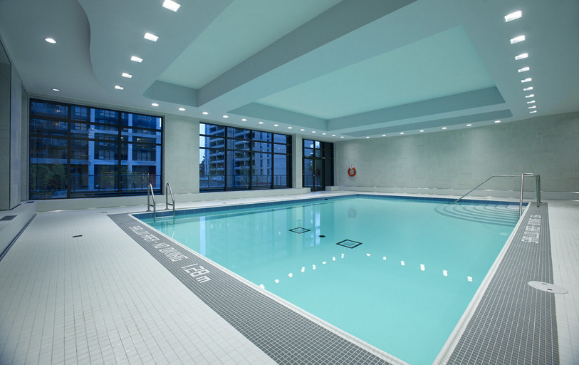 Indoor pool with a glass door to the outdoor sundeck furnished with patio seating located in Club Hampton by KG Group.