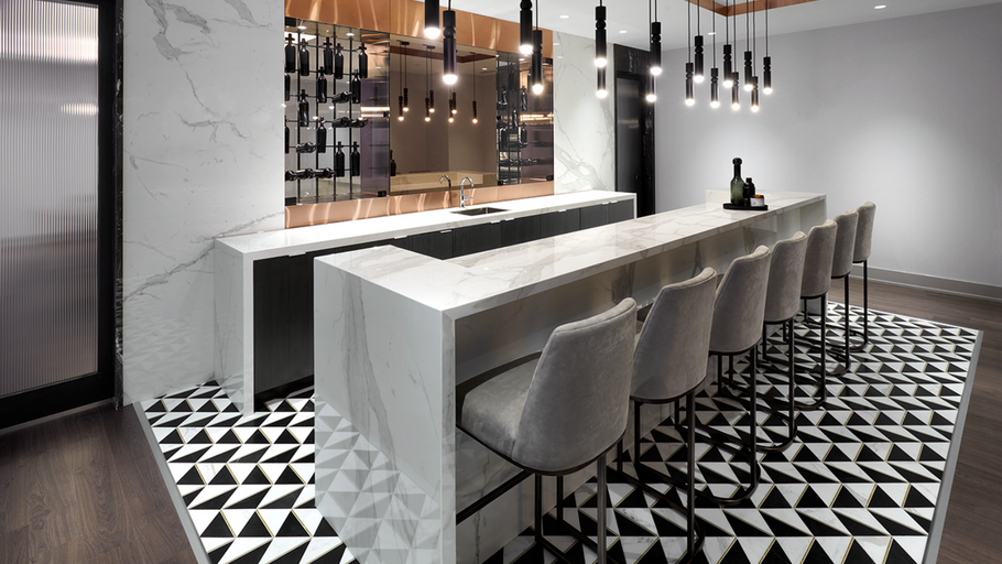 A luxurious bar with white marble finishes and high top chairs for socializing in a premium rental apartment building.