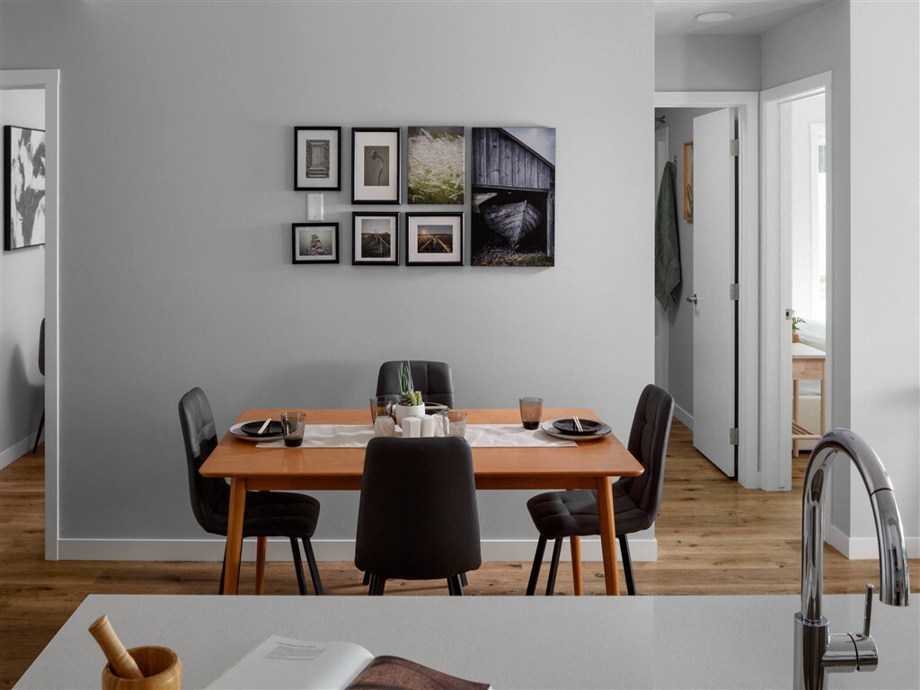 A dining room with a table set for two and a wall of framed pictures.
