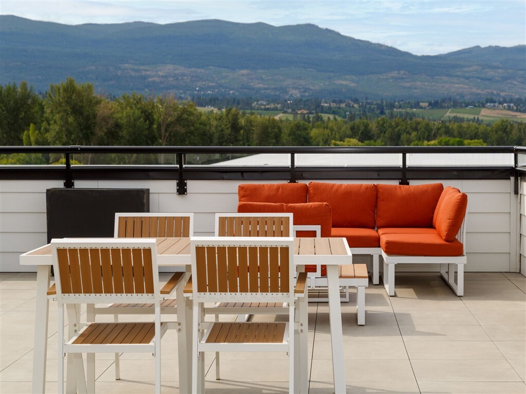 A white table and chairs with orange cushions on a balcony overlooking a valley.