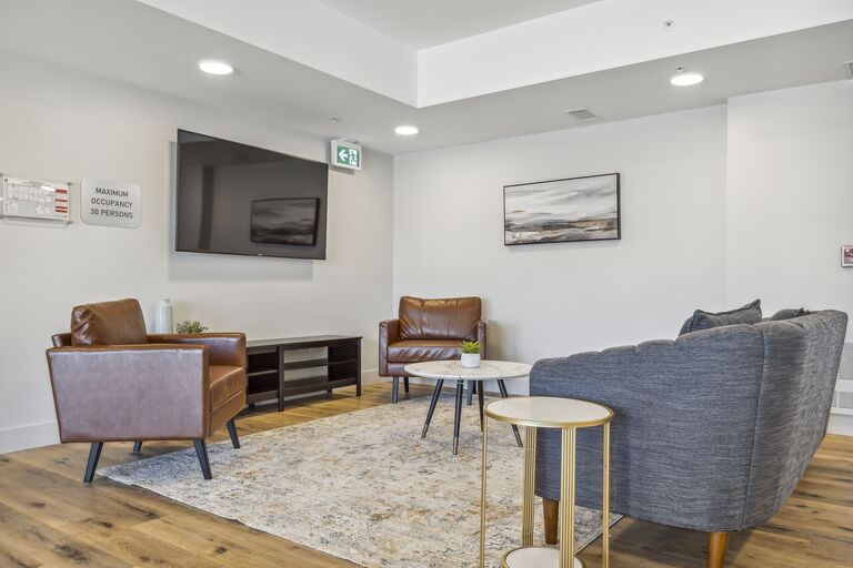 A living room with a grey couch, a brown chair, a brown leather chair, a brown side table, a grey armchair, a white side table, a white coffee table, a grey rug, a wooden floor, a white