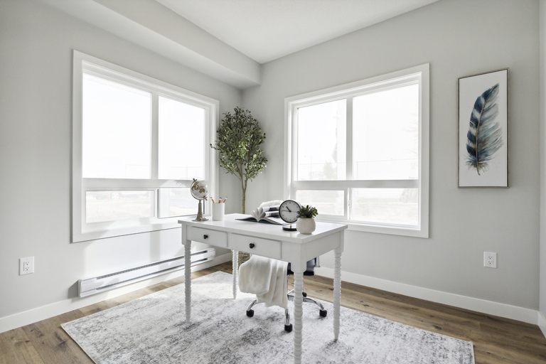 A white desk with a plant and a clock on it in a room with a large window.
