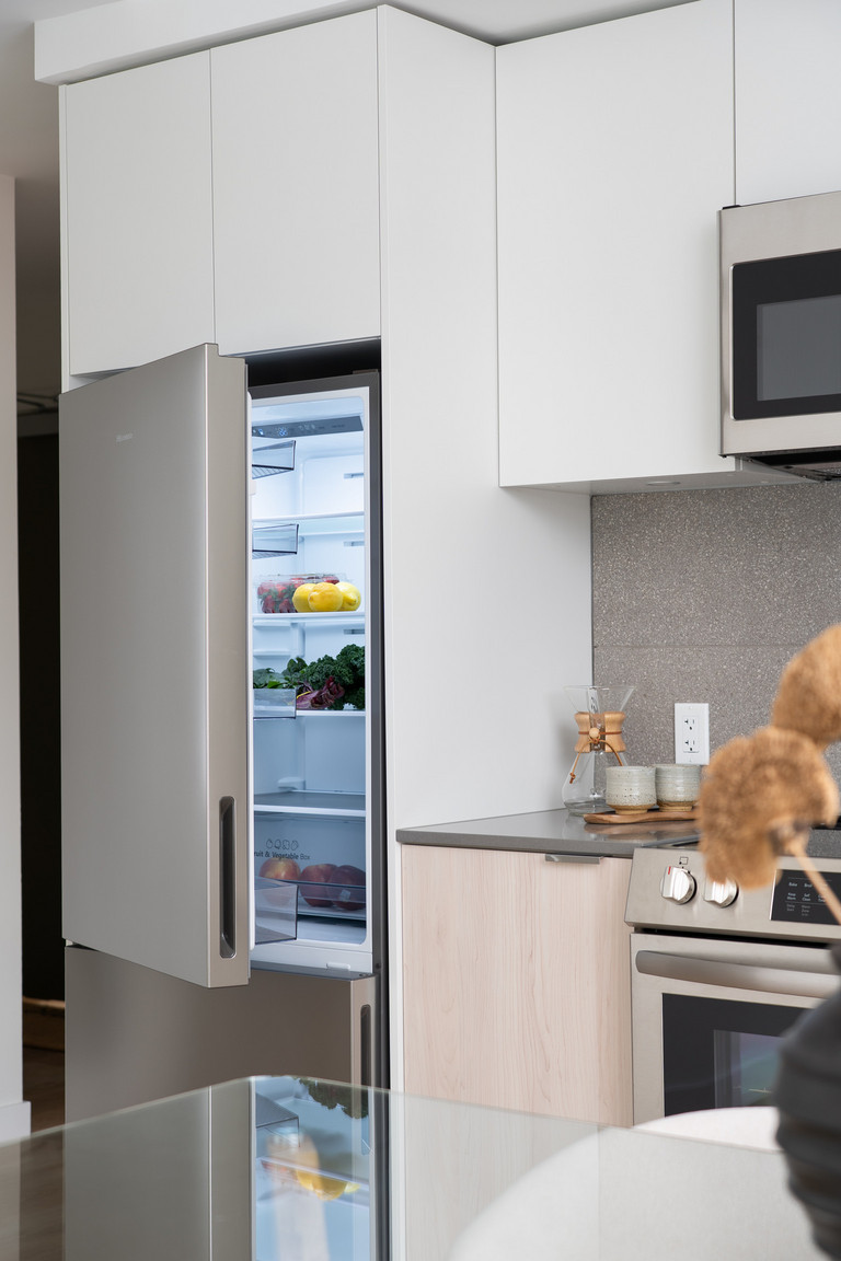 Bright and modern kitchen and dining area in an Eastward apartment, featuring stainless steel appliances including a refrigerator with its door slightly open, highlighting the contemporary design of these Vancouver rental homes.