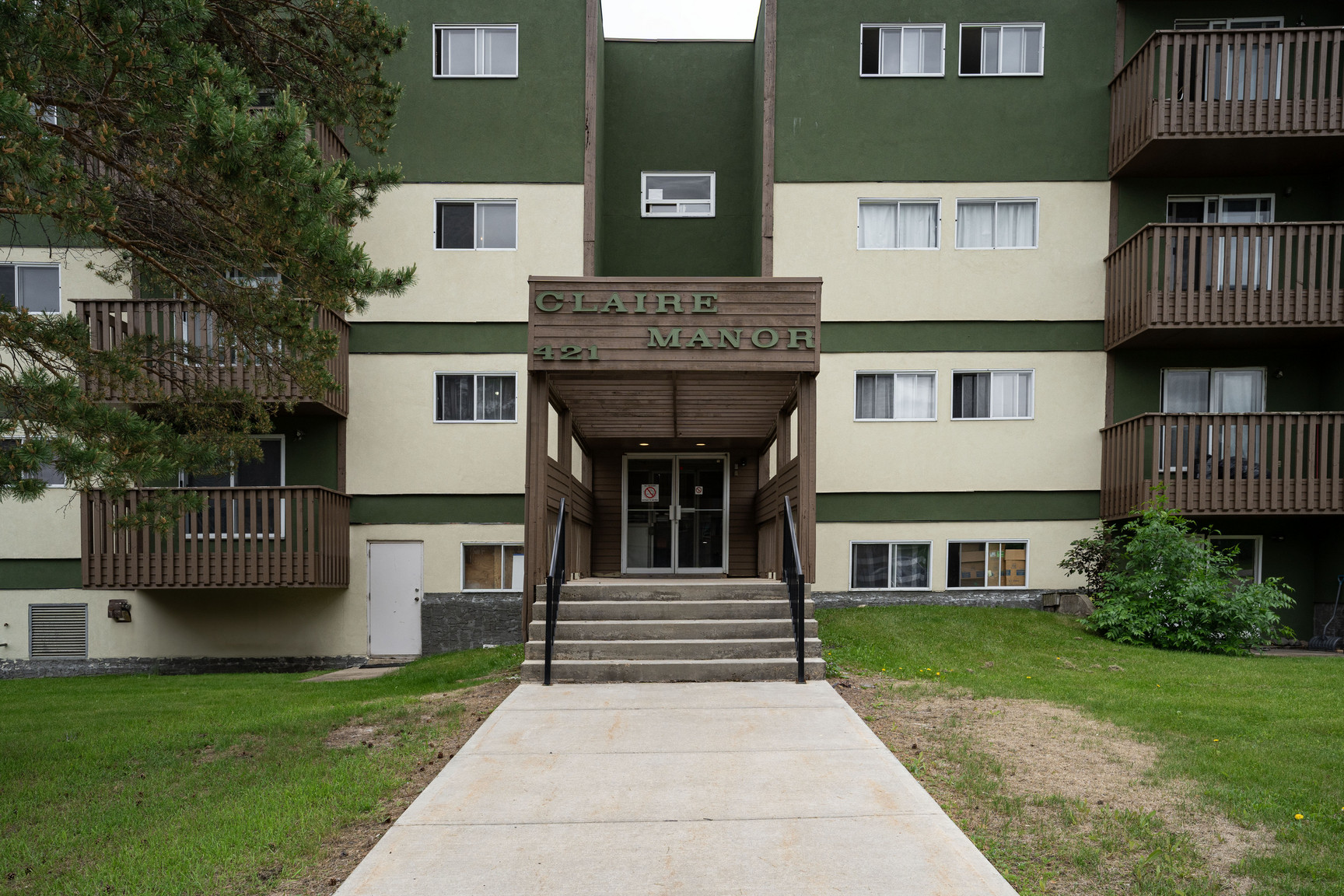 Claire Manor apartment building exterior in Fort McMurray featuring a four-story green and beige facade with balconies