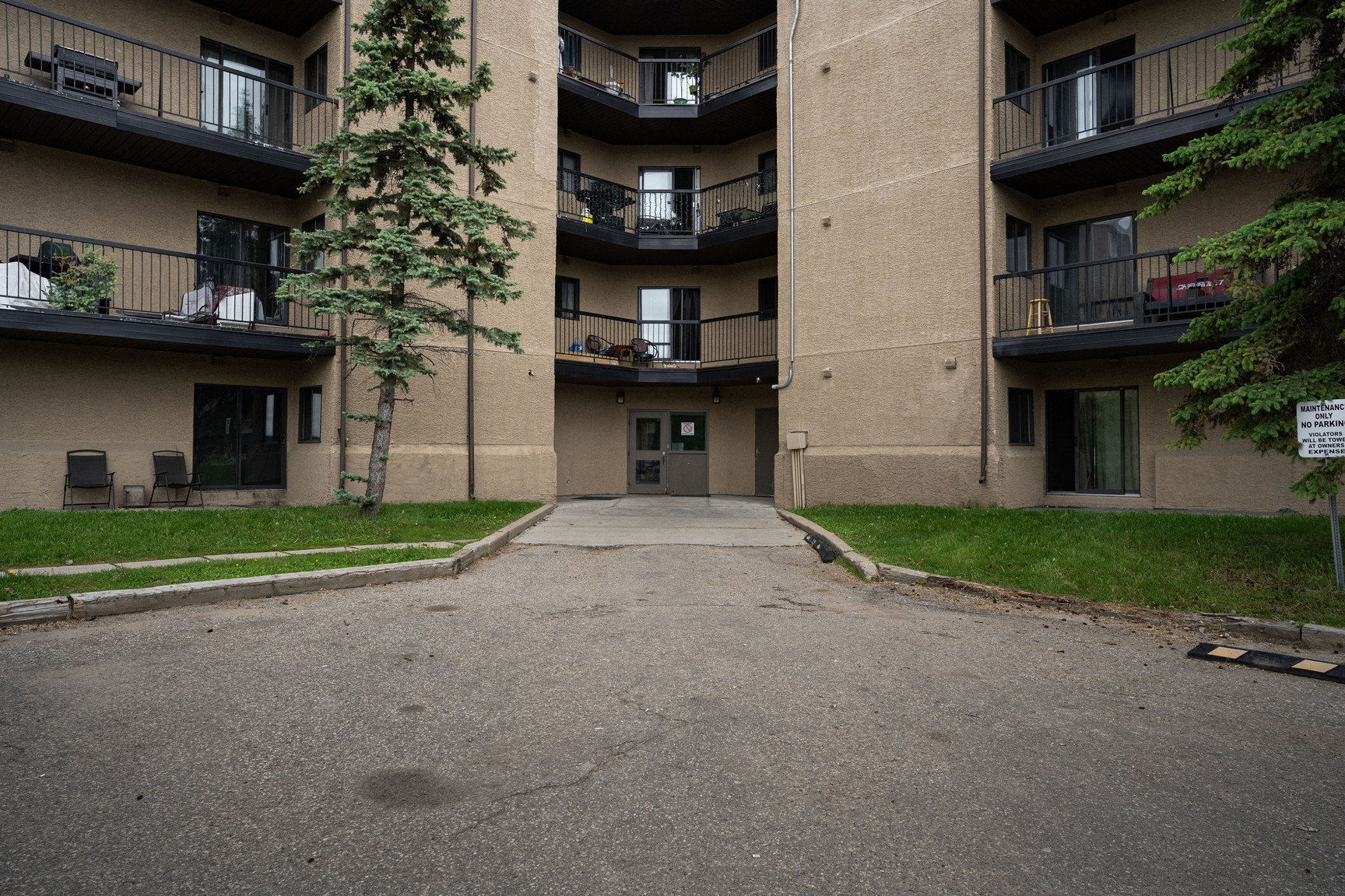 Exterior entrance of Rosedale Court apartments in Fort McMurray featuring a multi-story stucco building with private balconies and a paved driveway