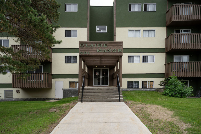 Claire Manor apartment building exterior in Fort McMurray featuring a four-story green and beige facade with balconies
