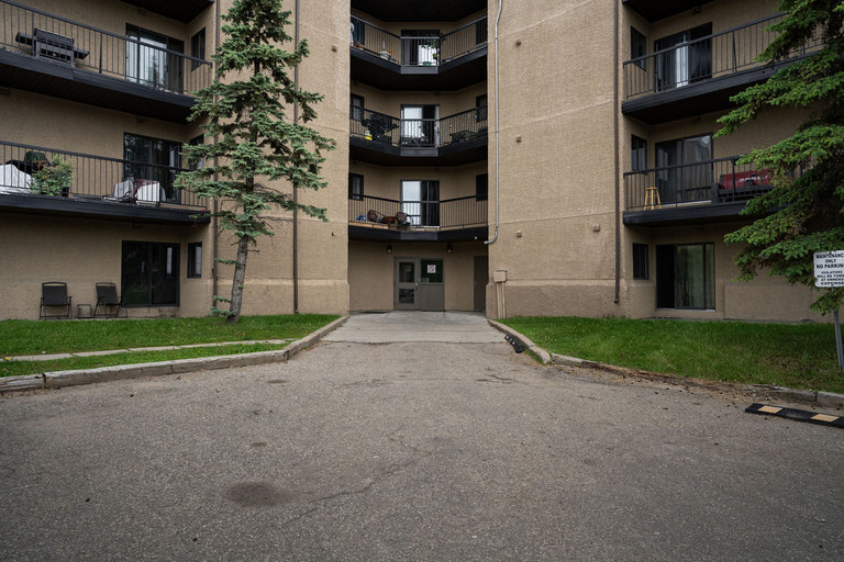 Exterior entrance of Rosedale Court apartments in Fort McMurray featuring a multi-story stucco building with private balconies and a paved driveway