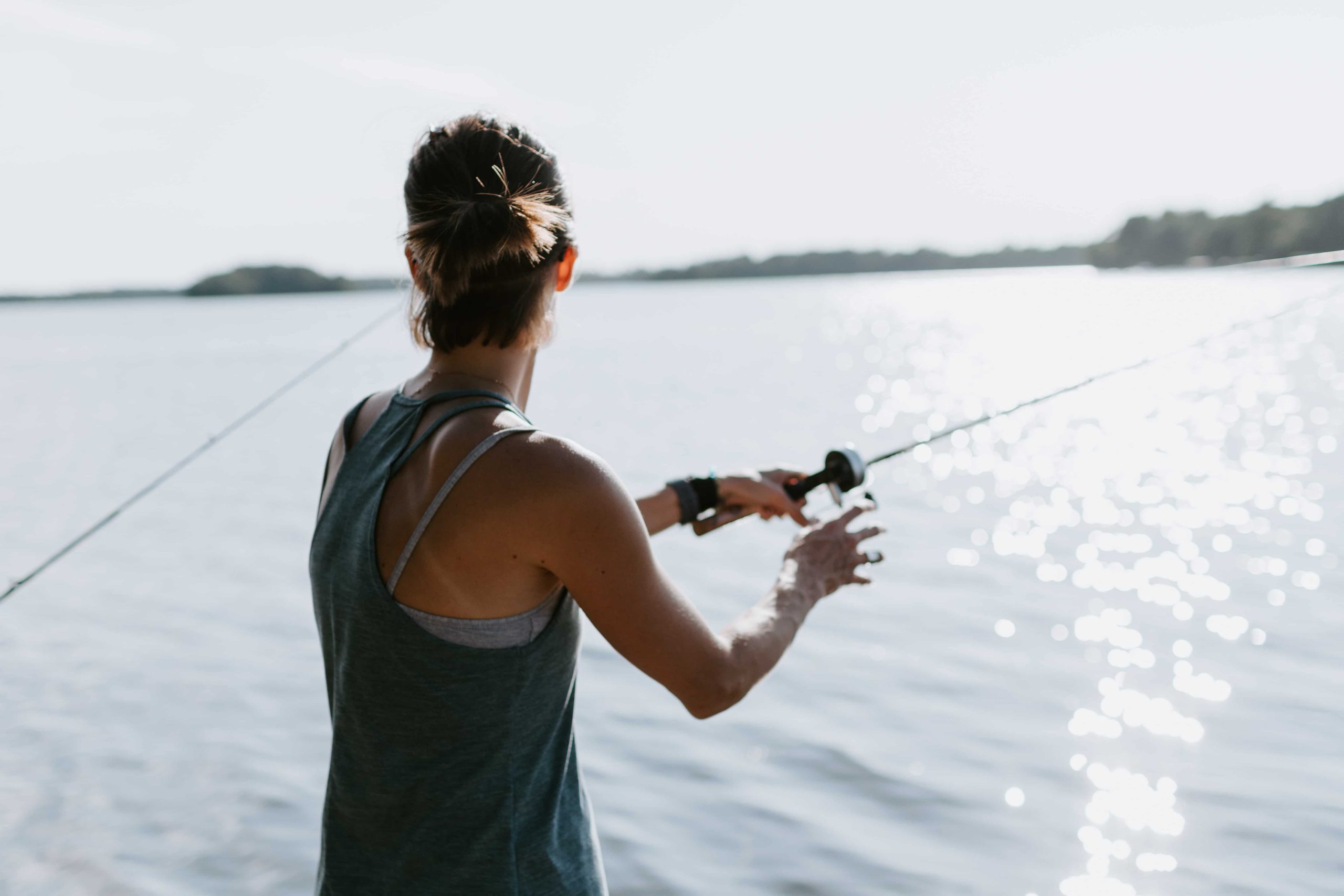 Woman in gray tank top with fishing rod standing on shore